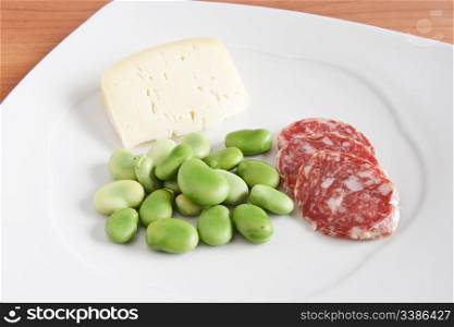 broad beans with pecorino cheese and salami slices on a white plate