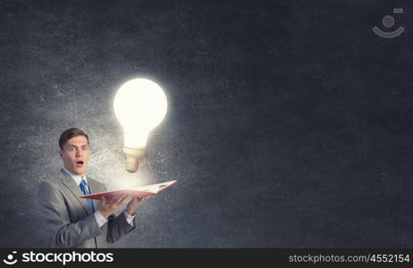 Broaden your mind. Businessman holding opened book with glass glowing light bulb