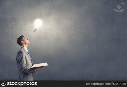 Broaden your mind. Businessman holding opened book with glass glowing light bulb