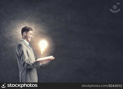 Broaden your mind. Businessman holding opened book with glass glowing light bulb