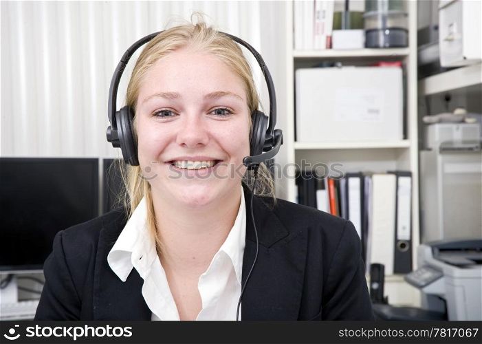 Broadly smiling receptionist in a small office wearing a head set