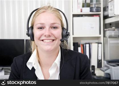 Broadly smiling receptionist in a small office wearing a head set