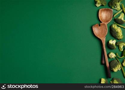 Broccoli and serving spoons on a green background. Top view of sliced seasonal vegetables. The concept of a healthy diet