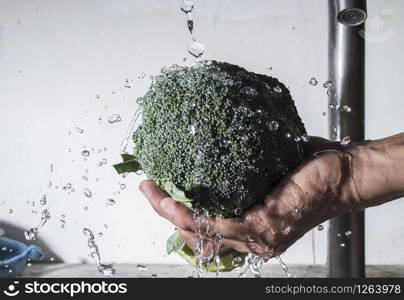 Broccoli on male hand cleaning with water splash