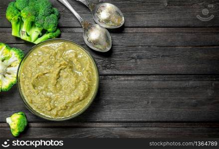 Broccoli puree with a spoon. On a wooden background.. Broccoli puree with a spoon.