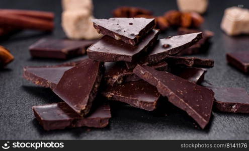 Broken black chocolate pieces with star anise and cinnamon on black background. Broken black chocolate pieces with star anise and cinnamon