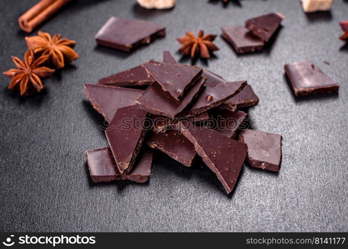 Broken black chocolate pieces with star anise and cinnamon on black background. Broken black chocolate pieces with star anise and cinnamon