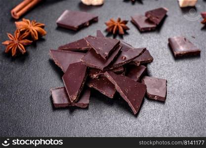 Broken black chocolate pieces with star anise and cinnamon on black background. Broken black chocolate pieces with star anise and cinnamon