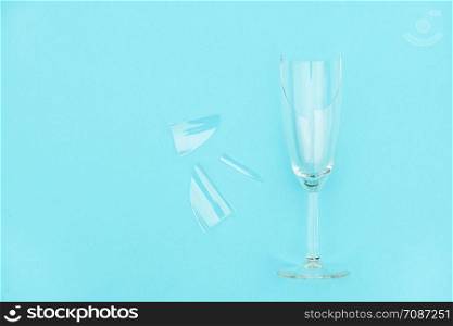 Broken champagne glass with splinters on blue background with copy space. Concept fight against alcoholism, drunkenness and refusal of alcohol. Creative Top view Flat lay.. Broken champagne glass with splinters on blue background with copy space. Concept fight against alcoholism, drunkenness and refusal of alcohol. Creative Top view Flat lay