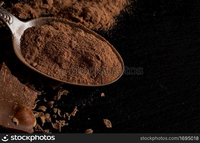 Broken chocolate nuts pieces and cocoa powder in spoon on dark background