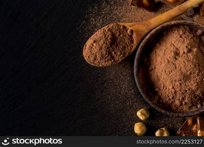 Broken chocolate nuts pieces and cocoa powder on dark background