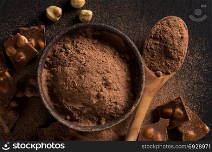 Broken chocolate nuts pieces and cocoa powder on dark background
