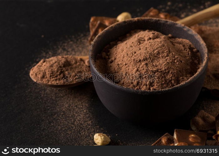 Broken chocolate nuts pieces and cocoa powder on dark background