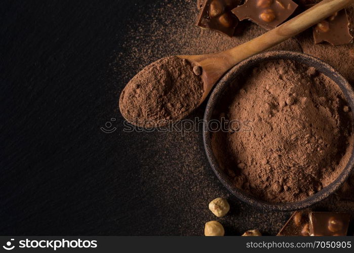 Broken chocolate nuts pieces and cocoa powder on dark background