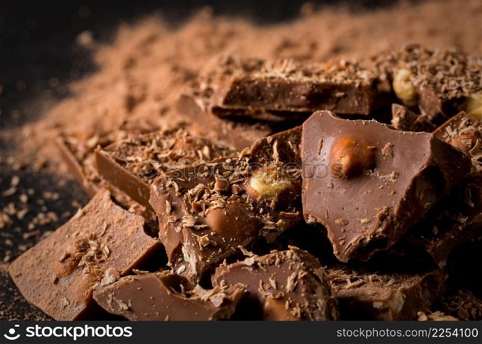 Broken chocolate nuts pieces and cocoa powder on dark stone background