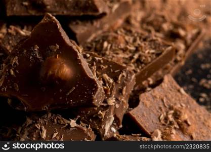 Broken chocolate nuts pieces and cocoa powder on dark stone background