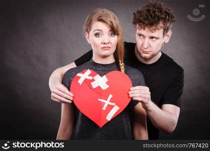 Broken heart difficult love concept. Sad unhappy couple woman and man holding paper red heart fixed with plaster bandage. Rift in relations.. Sad couple holds broken heart.
