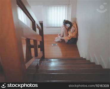 Broken heart love concept from Emotion feeling young asian girl sad listening to music sitting on stairs indoors at home. zoned out to music.
