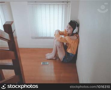 Broken heart love concept from Emotion feeling young asian girl sad listening to music sitting on stairs indoors at home. zoned out to music.
