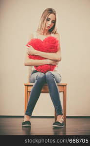 Broken heart love concept. Sad unhappy woman hugging red heart pillow