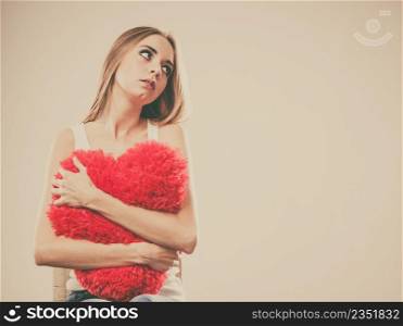 Broken heart love concept. Sad unhappy woman hugging red heart pillow closeup