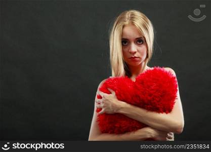 Broken heart love concept. Sad unhappy woman hugging red heart pillow dark background