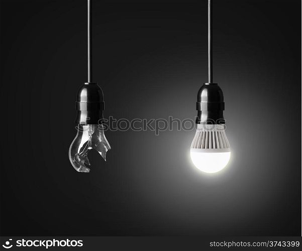 Broken light bulb and glowing LED bulb on black