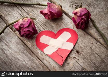 Broken paper heart and old roses on wooden background