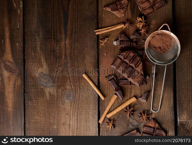 broken pieces of dark chocolate, cinnamon sticks and star anise on a brown wooden table, top view. Copy space