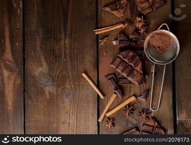broken pieces of dark chocolate, cinnamon sticks and star anise on a brown wooden table, top view. Copy space