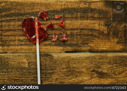Broken red lollipo with heart shape on a wooden background