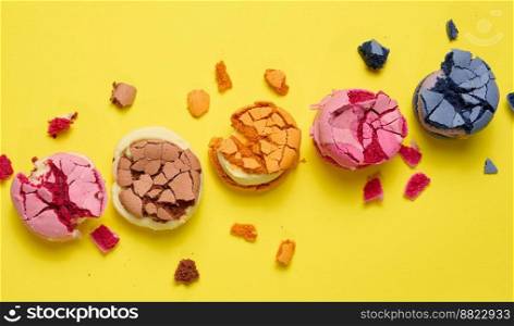Broken round macarons with crumbs on a yellow background, delicious dessert, top view