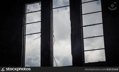 Broken window in an abandoned building - View from inside - sky with clouds seen through the window.