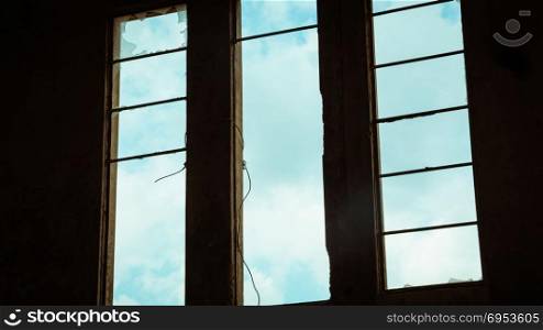 Broken window in an abandoned building - View from inside - sky with clouds seen through the window.