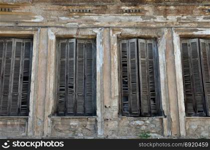 Broken wooden window shutters and chipped wall of a decayed building.