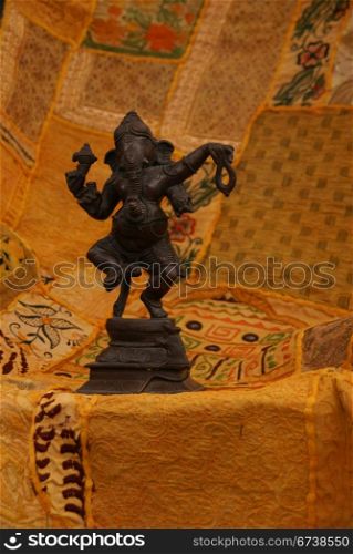 Bronze Ganesha dancing, on yellow - orange Rajasthani textile backdrop made from saris. [Ganesha, the son of Shiva and Parvati, the elephant headed god, is worshipped as the lord of beginnings and as the lord of obstacles, patron of arts and sciences, and the god of intellect and wisdom ]