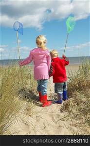 Brother and sister (4-6) with fishing nets standing on sand dunes