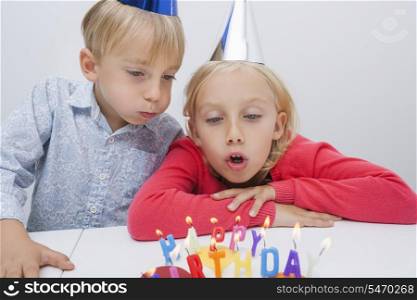 Brother and sister blowing birthday candles at table in house