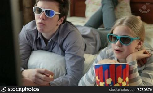 Brother and sister eating popcorn and watching 3D TV movie at home