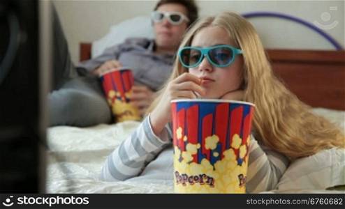 Brother and sister eating popcorn and watching 3D TV movie at home