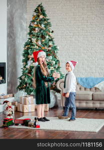 Brother and sister give and unpack gifts under the Christmas tree, sitting by the fireplace, on Christmas morning. Merry Christmas.. Brother and sister give and unpack gifts under the Christmas tree, sitting by the fireplace, on Christmas morning.