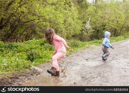 Brother and sister having fun splashing in a mud puddle. Games for yard