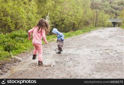 Brother and sister having fun splashing in a mud puddle. Games for yard