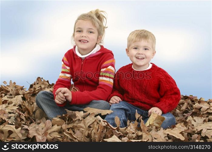 Brother and Sister in red sweaters sitting in big pile of leaves.