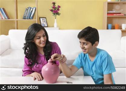 Brother and sister inserting a coin into a piggy bank
