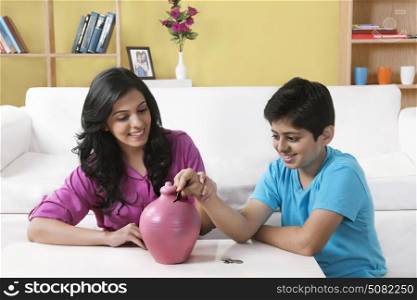 Brother and sister inserting a coin into a piggy bank