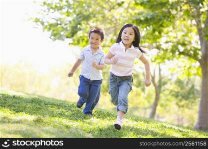 Brother and sister running outdoors smiling