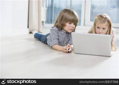 Brother and sister using laptop on floor at home