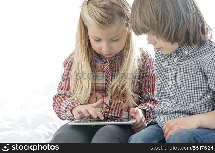Brother and sister using tablet PC in bedroom