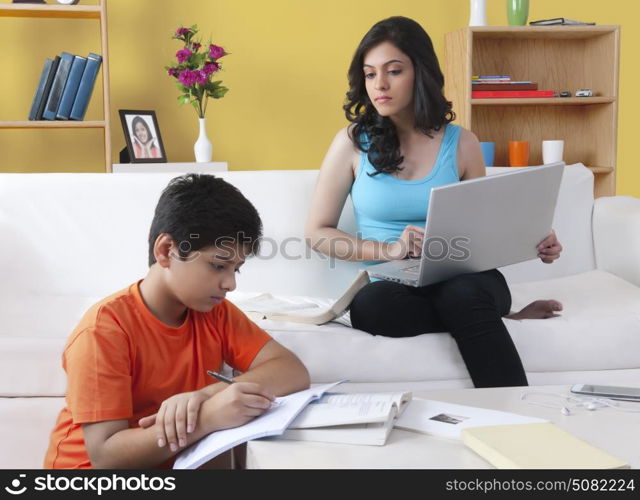 Brother doing homework while his sister using laptop